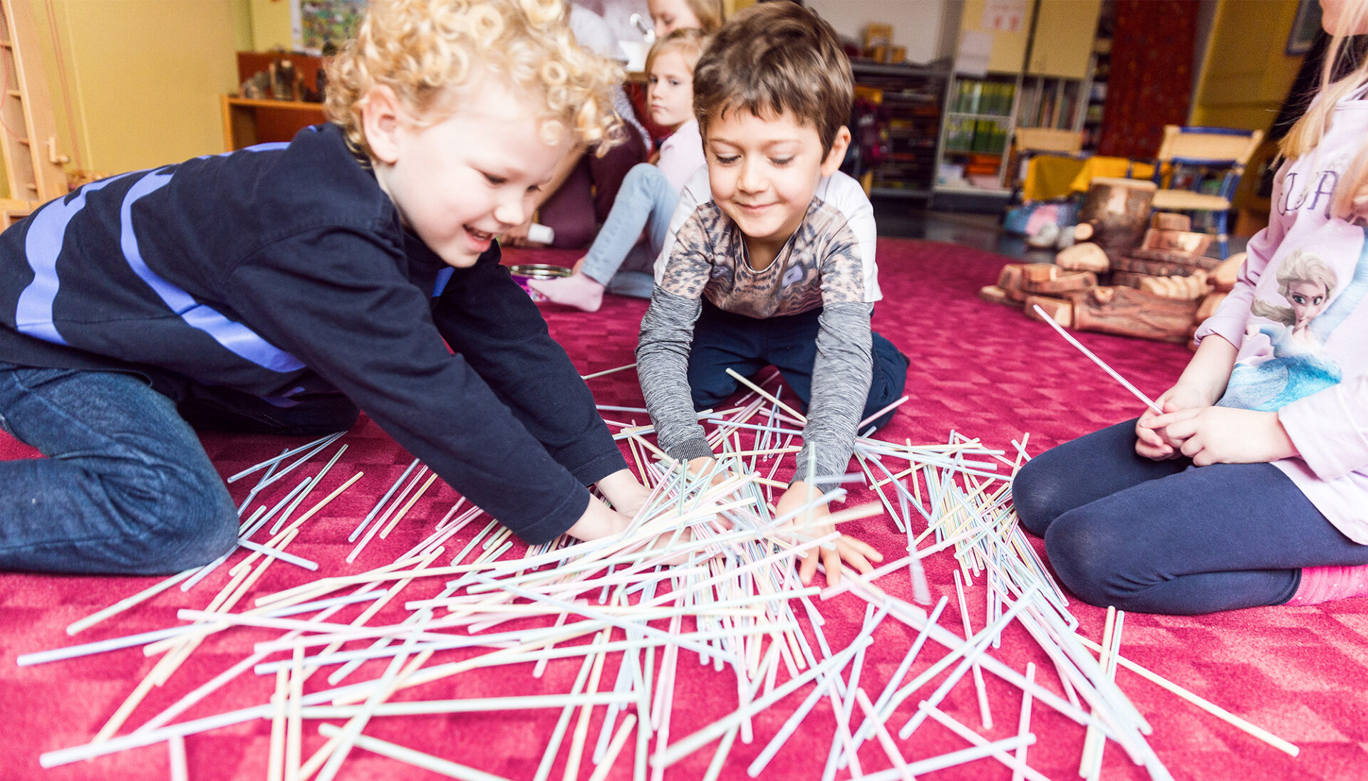 Drei Kinder spielen mit einer großen Menge an Plastikstrohhalmen