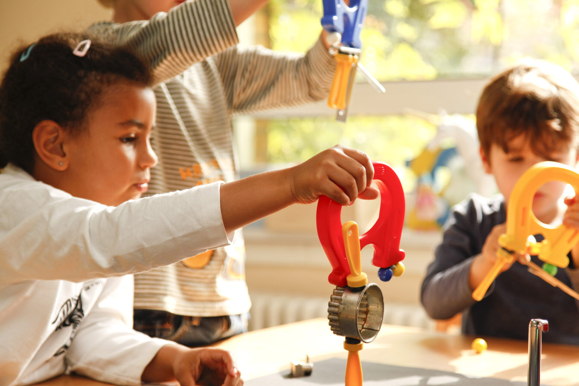 Drei Kinder halten starke Magnete hoch, an denen verschiedene Dinge sowie weitere Magnete hängen