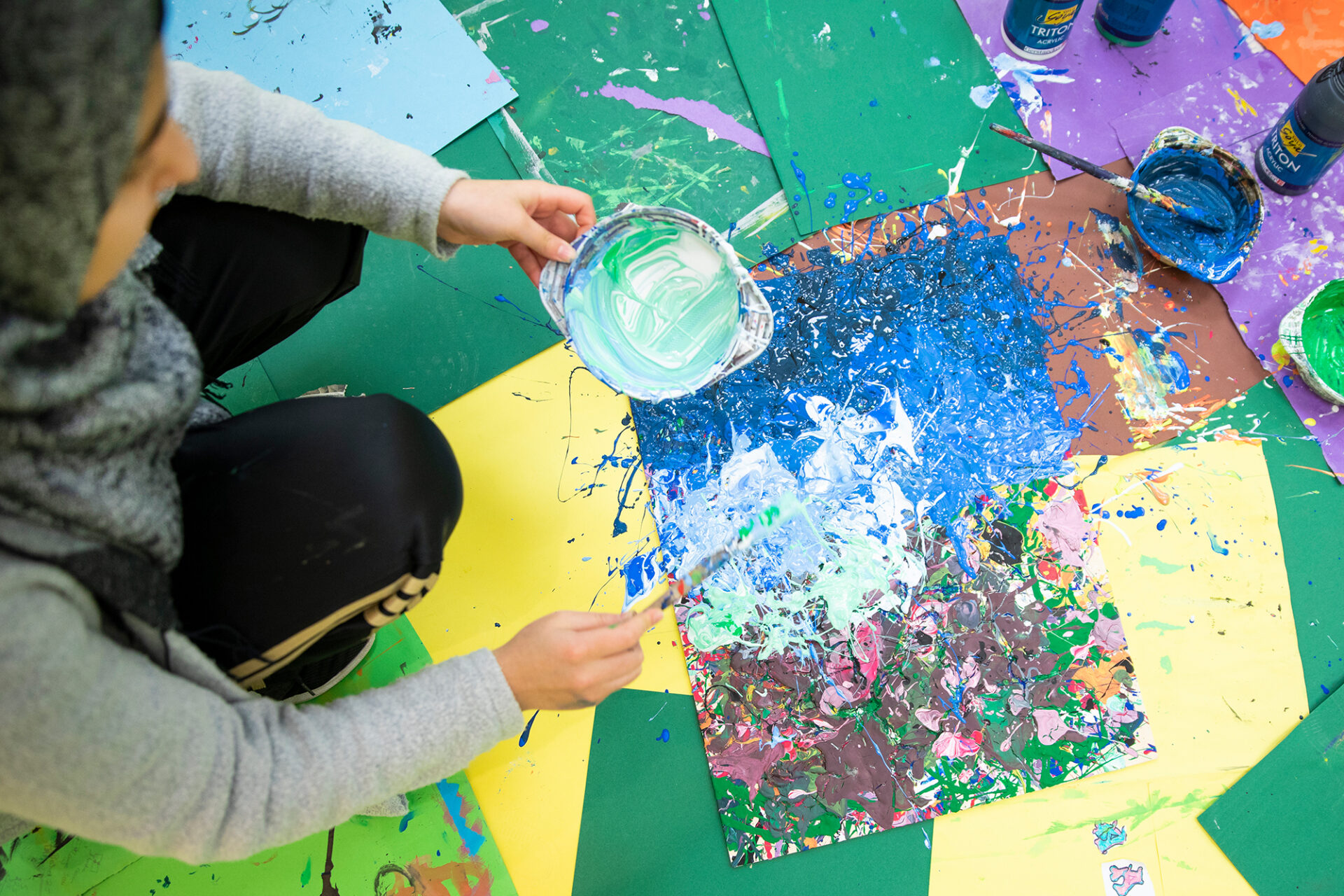 Ein Kind malt mit dickflüssigen Farben auf buntem Papier